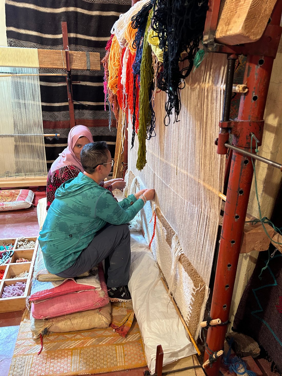 A traveler learning traditional carpet weaving from a local Moroccan artisan